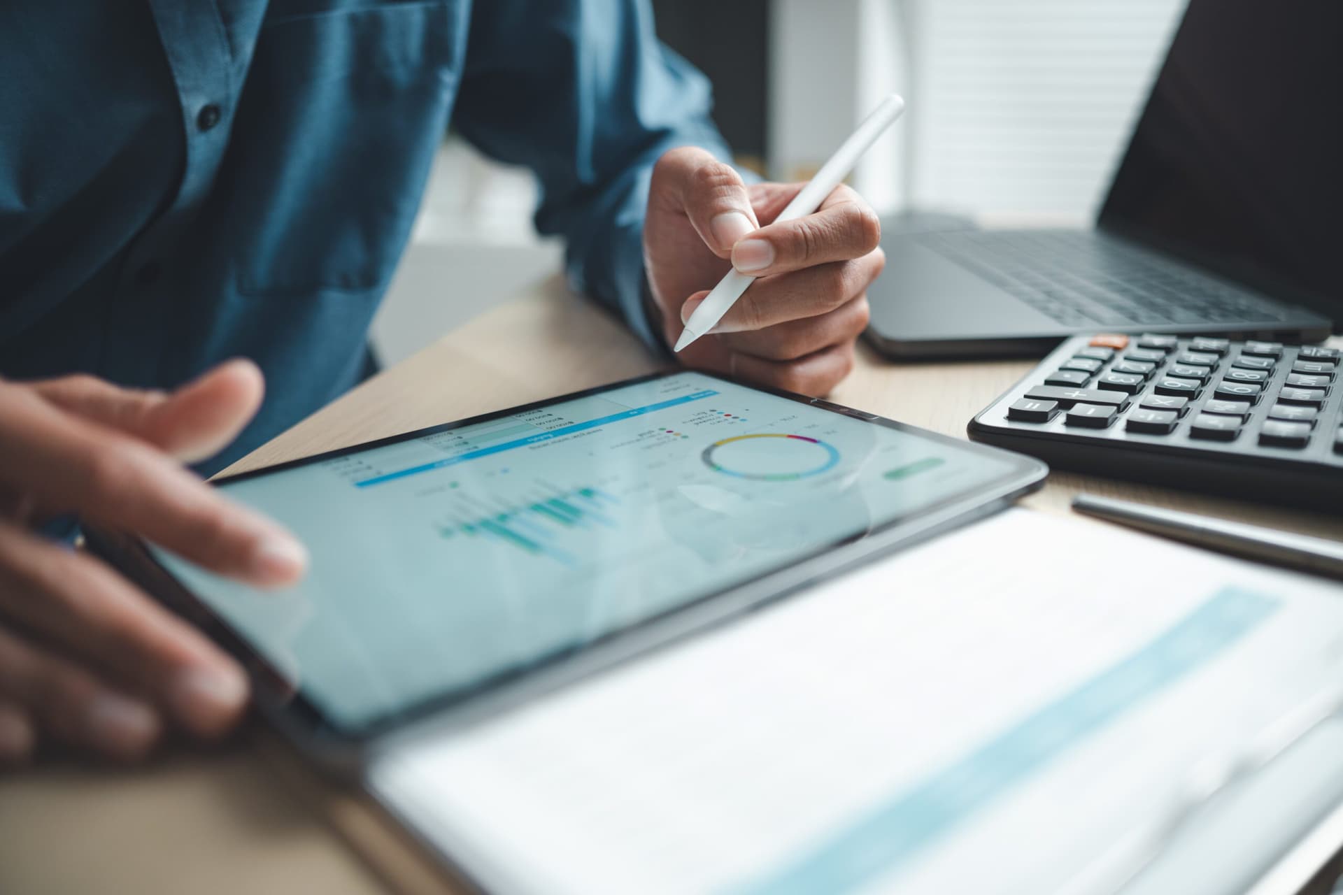 Business professional analyzing financial data on digital tablet dashboard with calculator and laptop, representing accounting software, ERP system integration, performance monitoring.